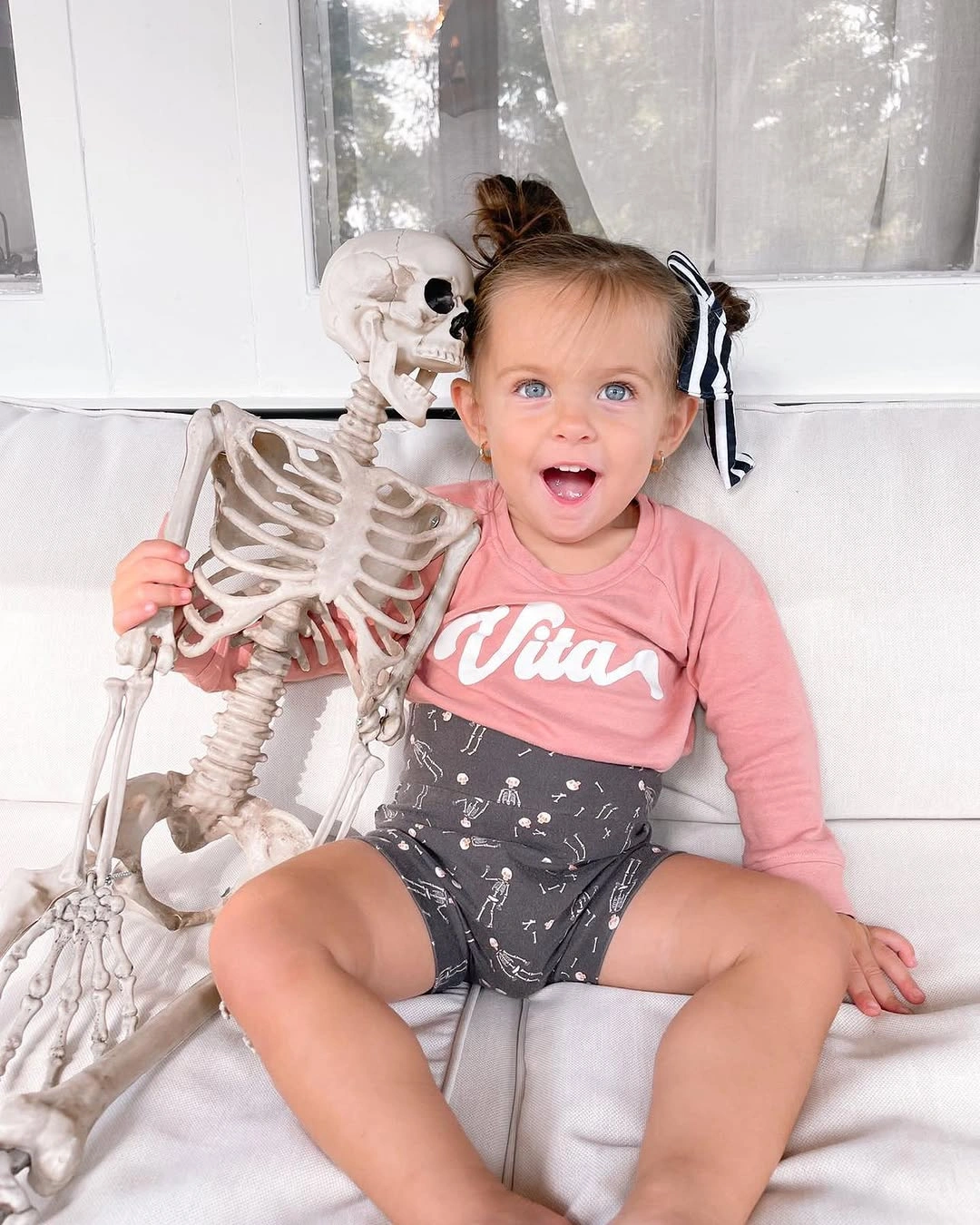 Toddler in pink and gray clothes holding a small skeleton prop