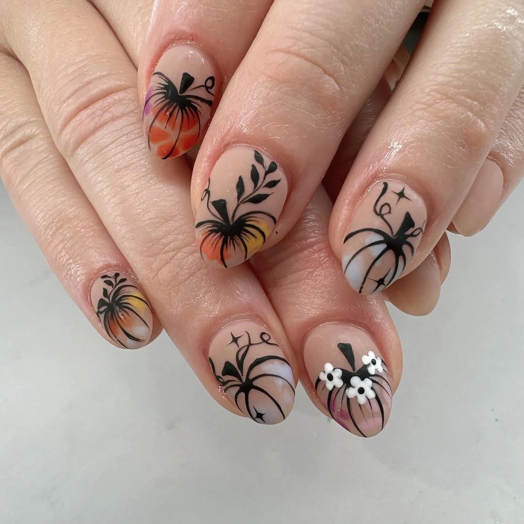 Sheer nude almond nails with thin black webs and orange pumpkins