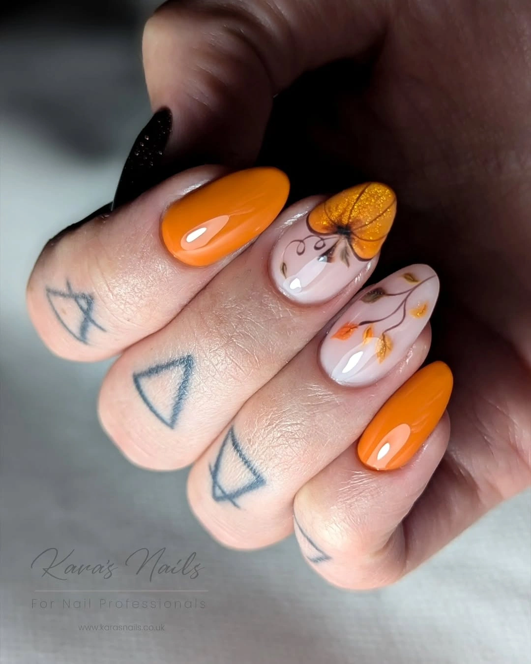 Orange almond nails with fine pumpkin line art and shimmer accent