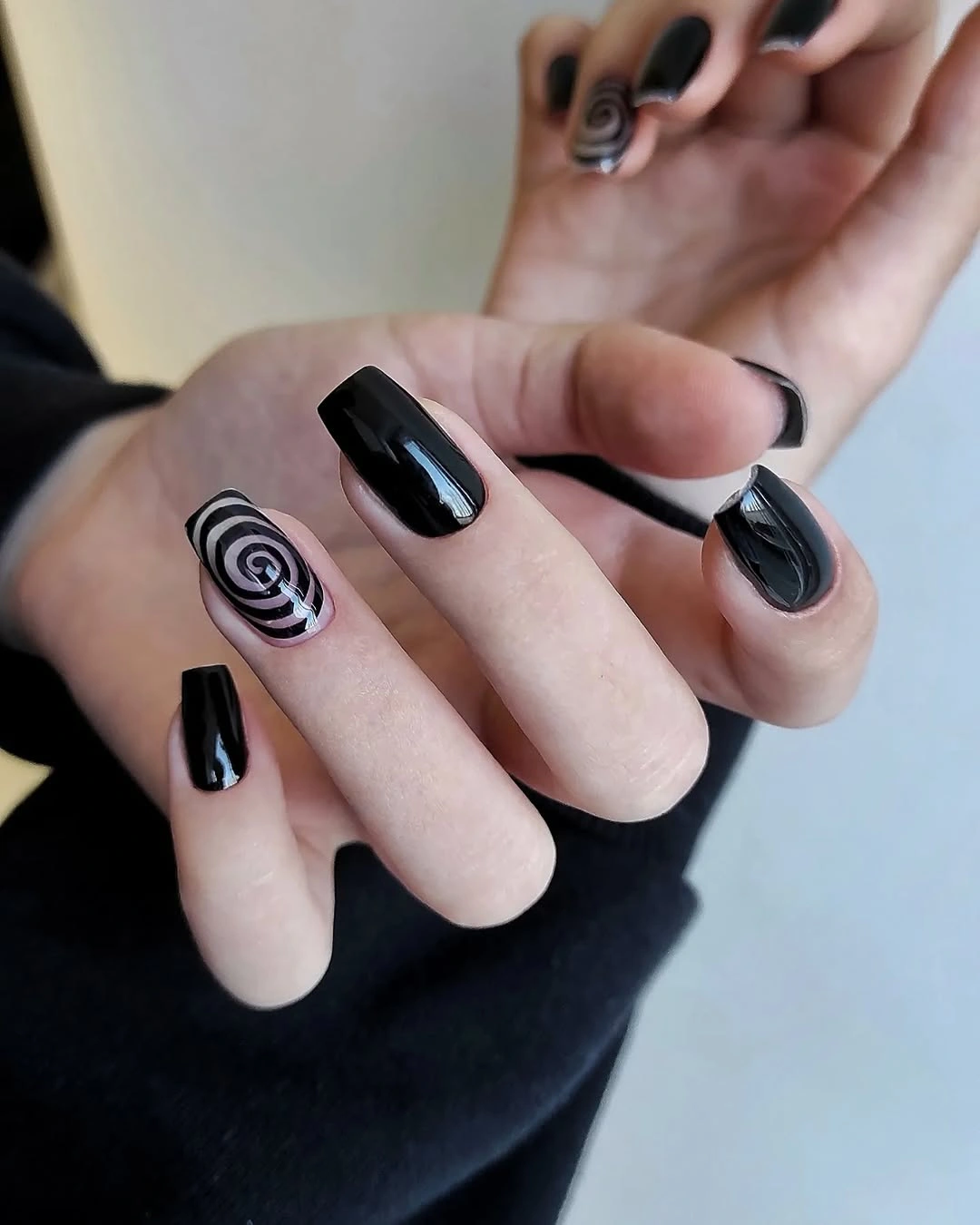 Short glossy black nails with one bold white spiral accent