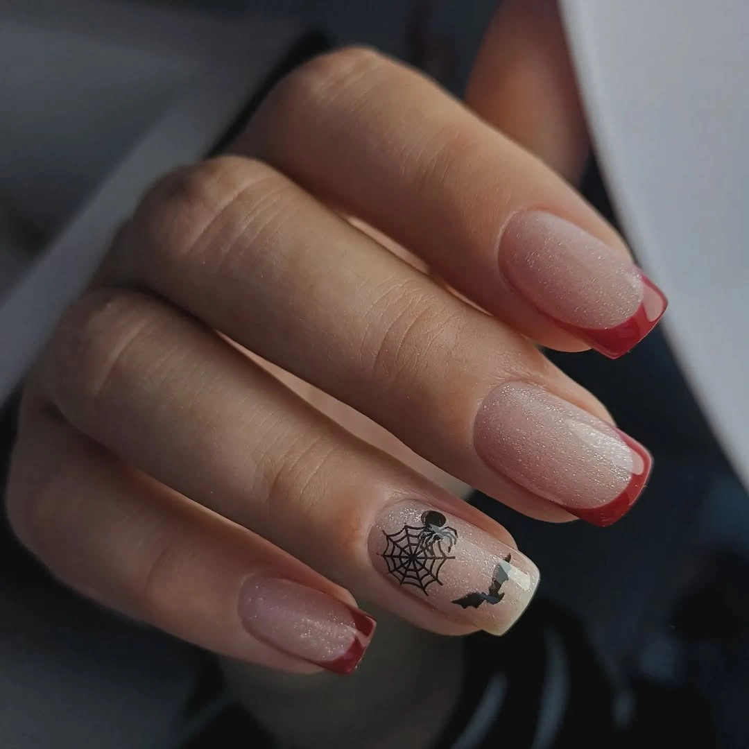 Short almond nude nails with red tips and tiny black web art