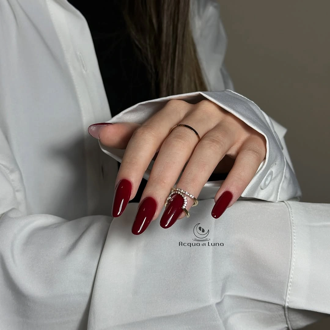 Long glossy burgundy almond nails contrasted with a crisp white sleeve