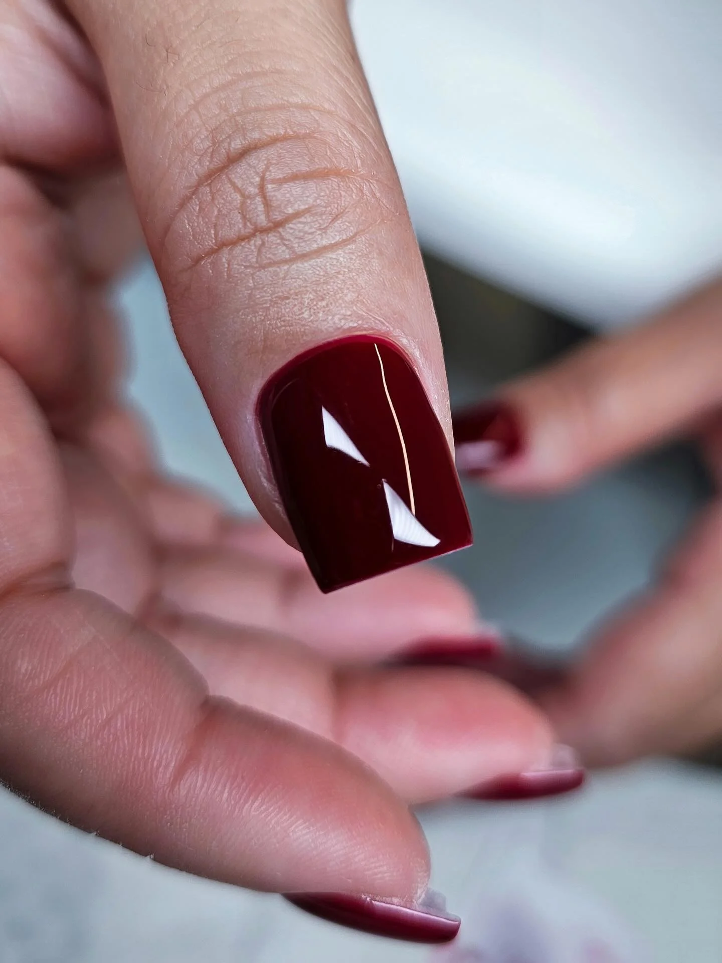 Short square nail in a dark glossy red-brown burgundy finish
