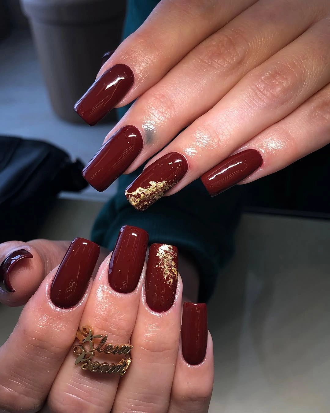Long burgundy square nails with a textured gold accent at one tip