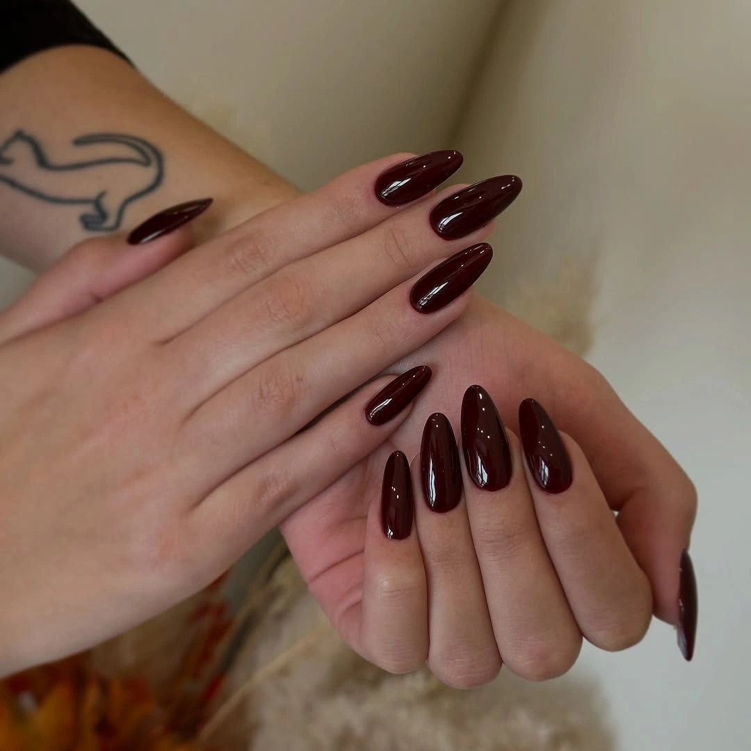 Long glossy almond nails in a deep oxblood burgundy shade