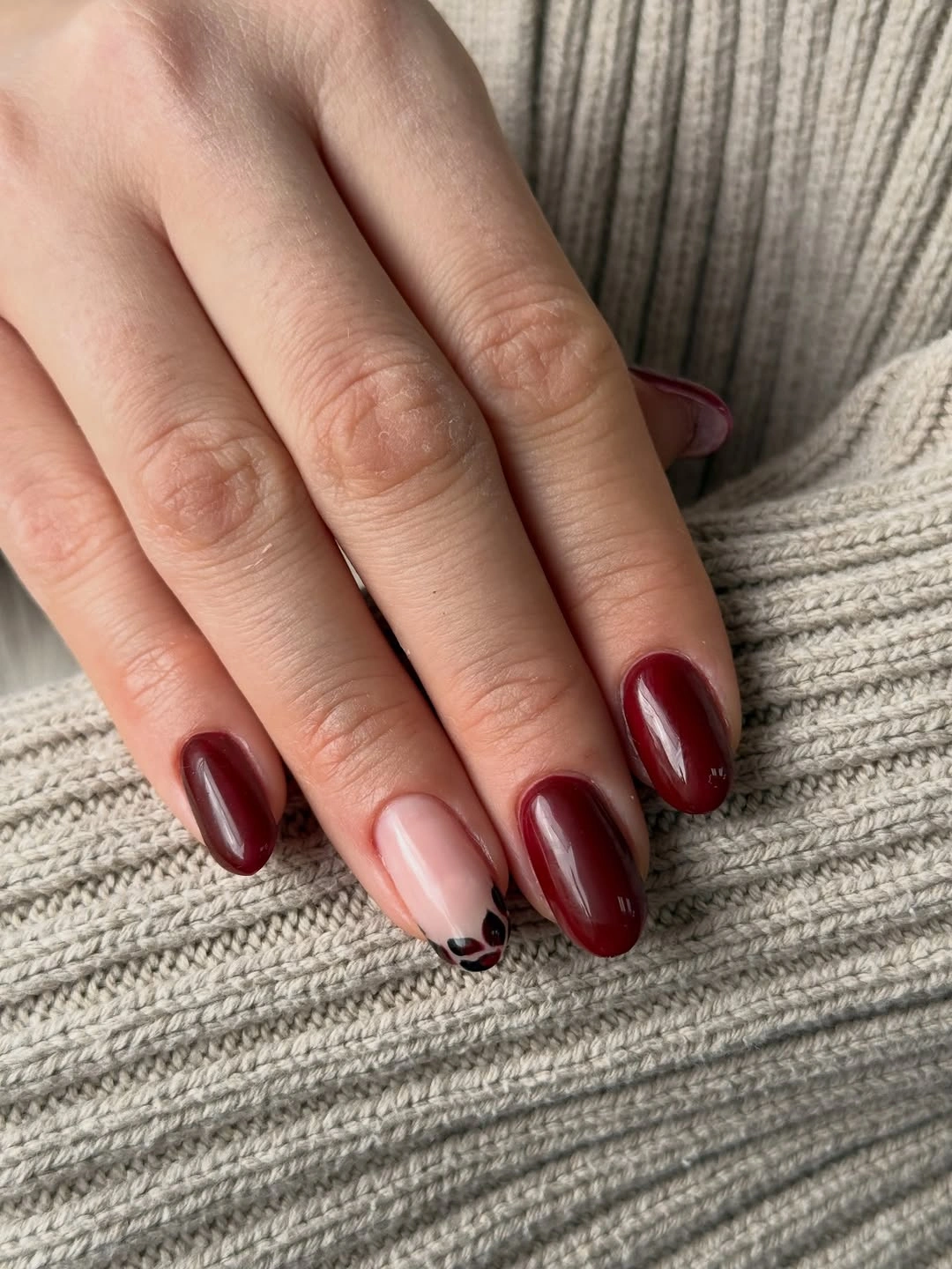 Nude pink almond nails with burgundy tips and small dark spotted accents