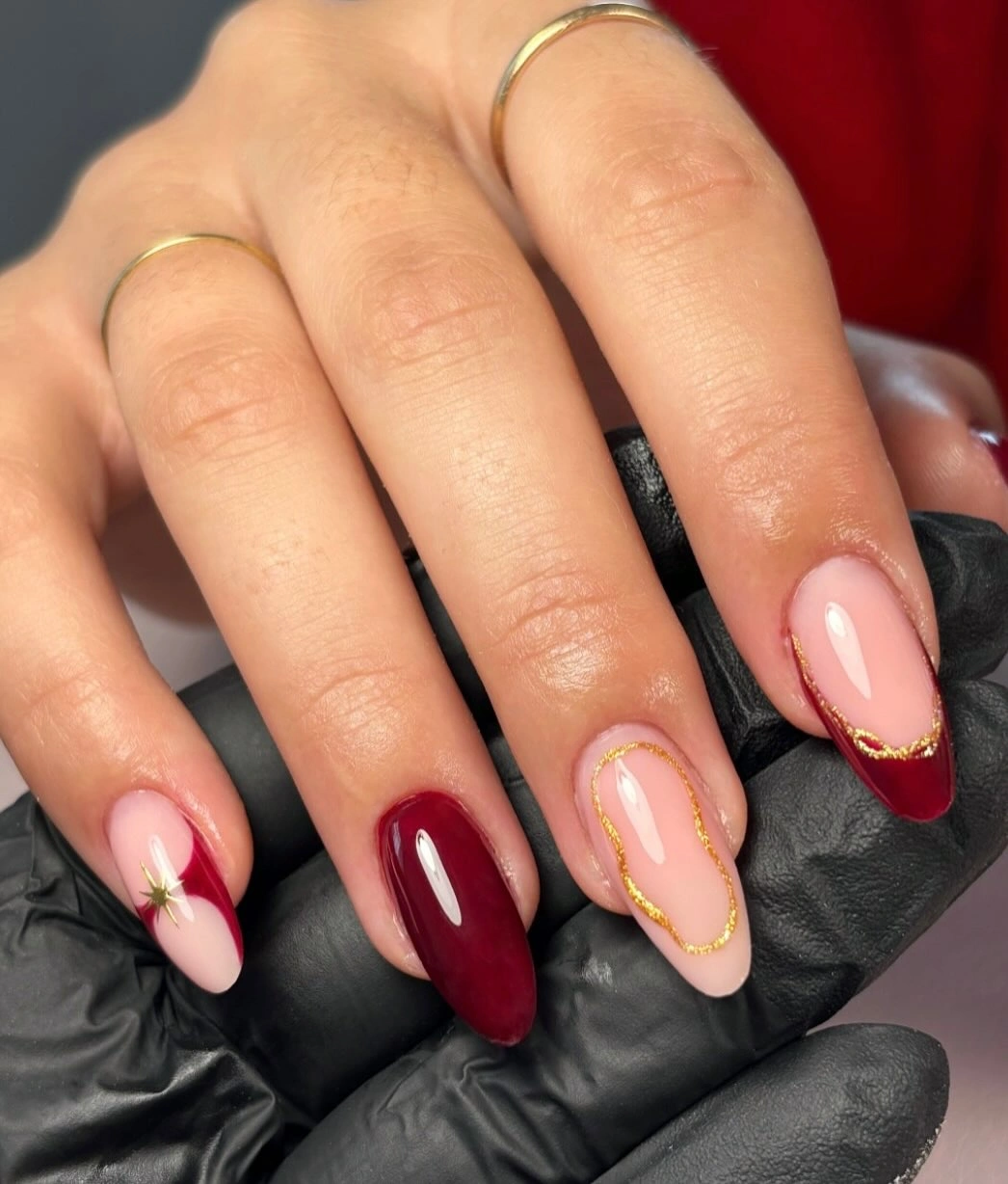 Pale pink and burgundy almond nails with thin curved gold line accents