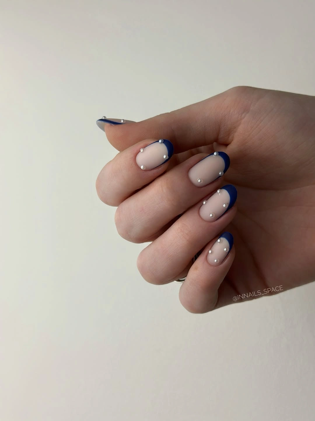 Nude almond nails with slim navy French tips and tiny studs