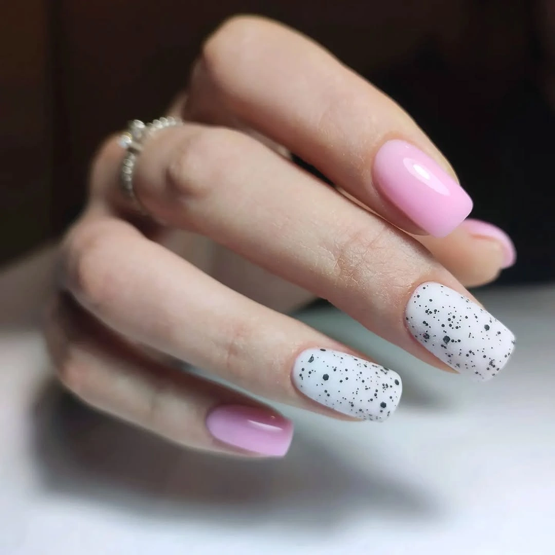 Pink and white square nails with scattered black speckle details