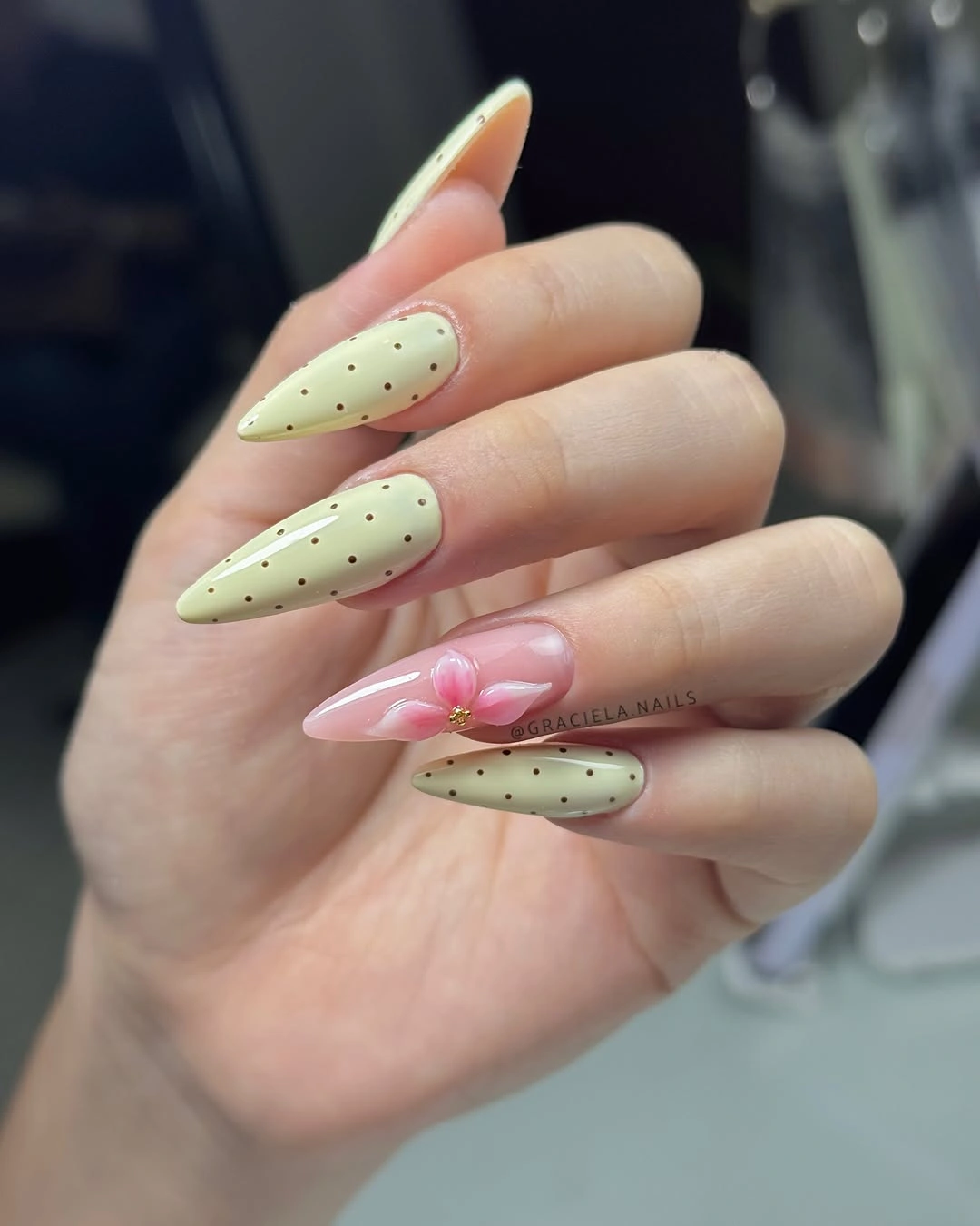 Pale green almond nails with black dots and one pink floral accent