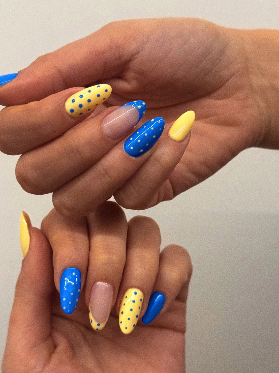 Bright cobalt and yellow almond nails with white dots and nude accent