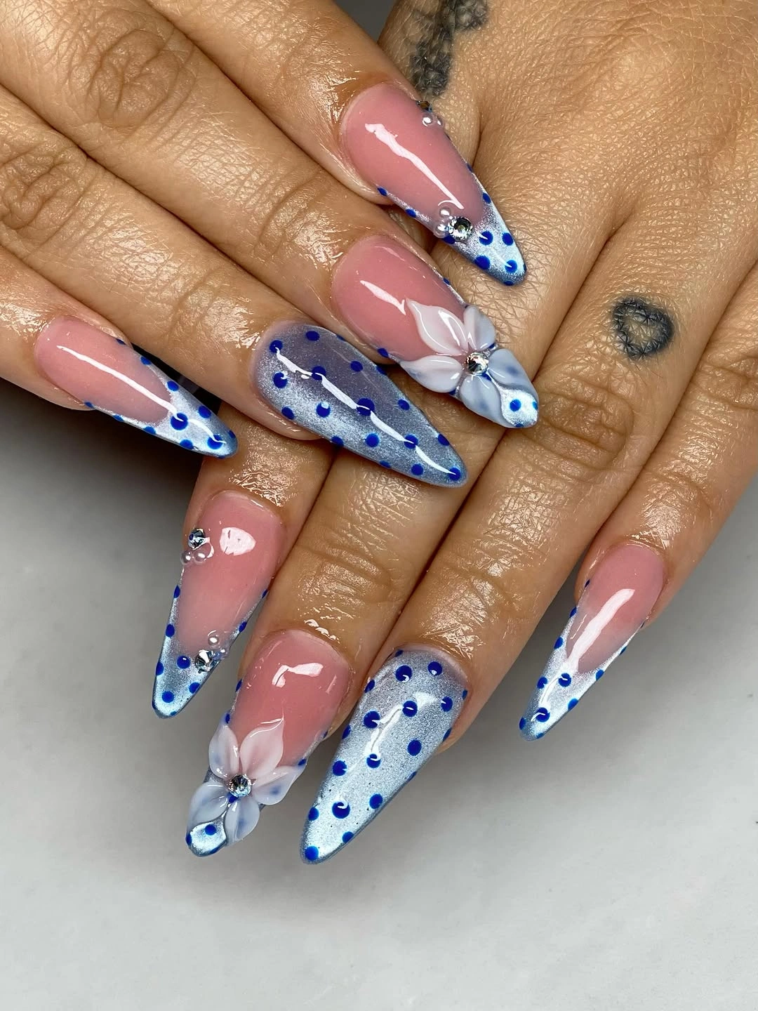 Nude stiletto nails with cobalt dotted tips and small white floral accents