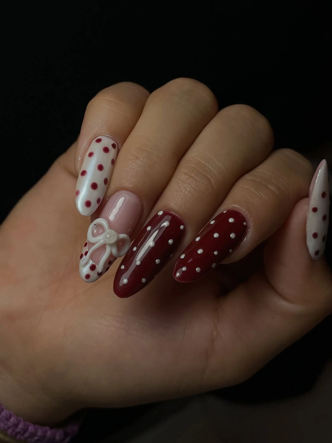 Burgundy pink and white almond nails with dots and a small bow accent