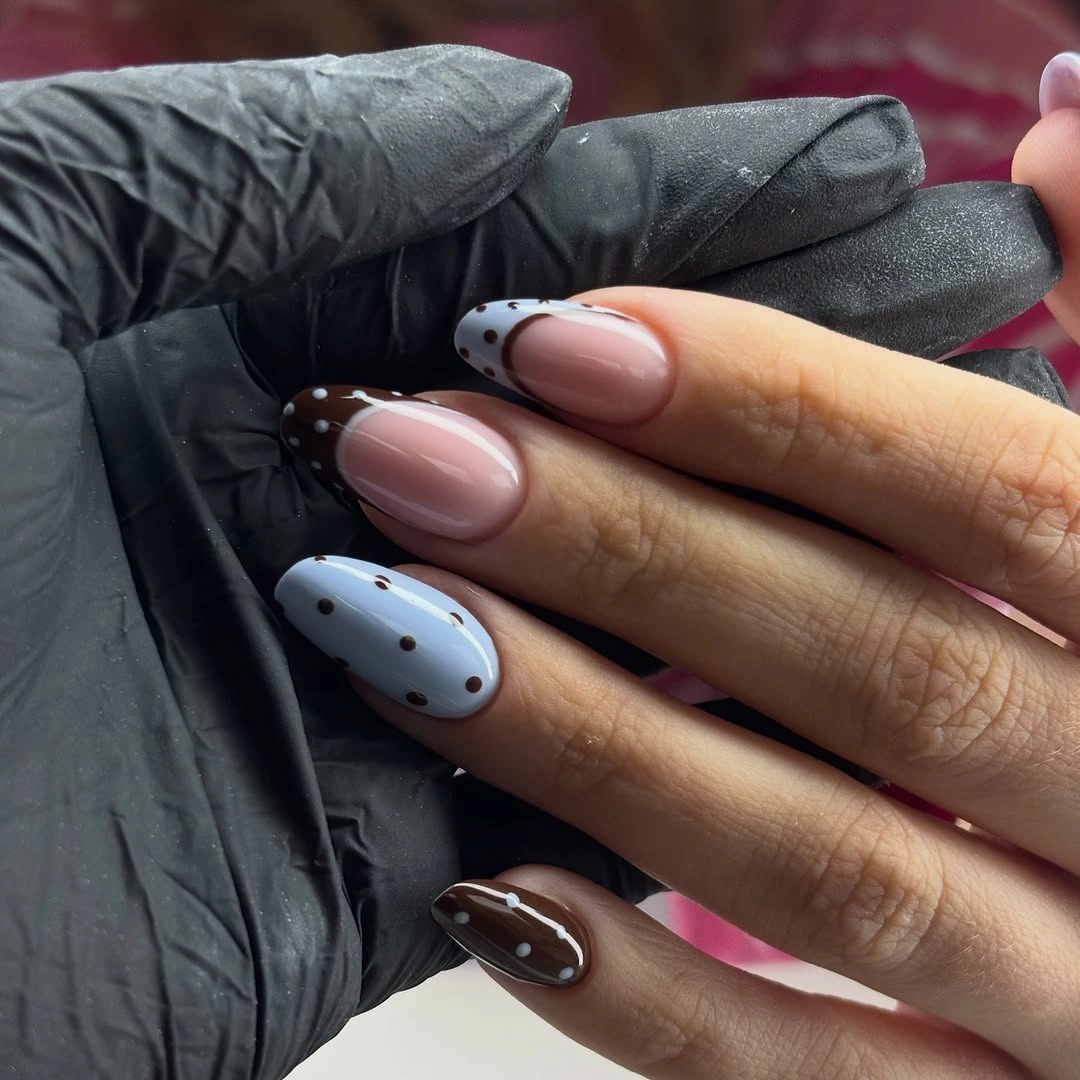 Nude almond nails with chocolate curved tips and a pale blue dotted accent