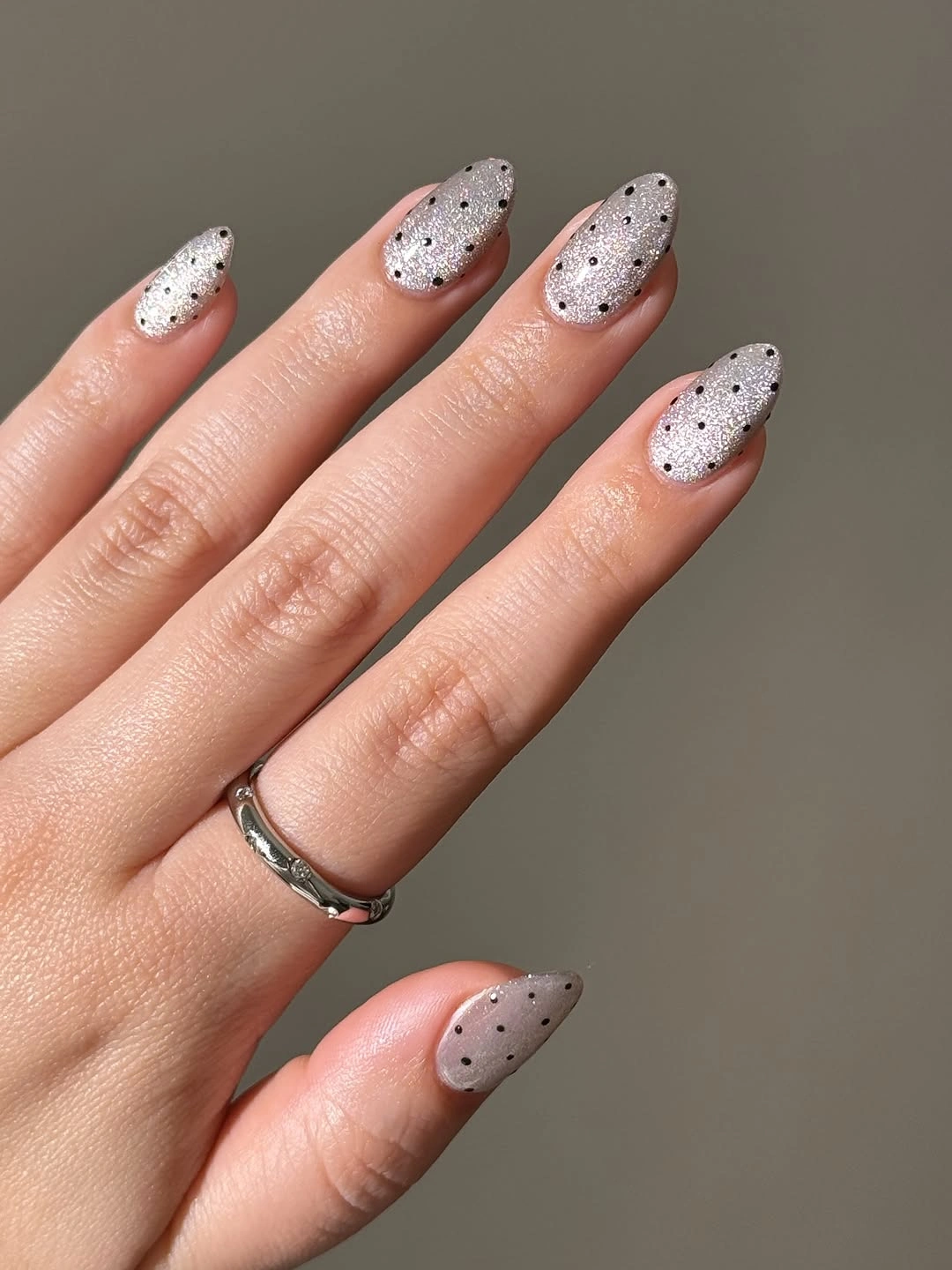 Neutral taupe almond nails with small scattered black speckle dots