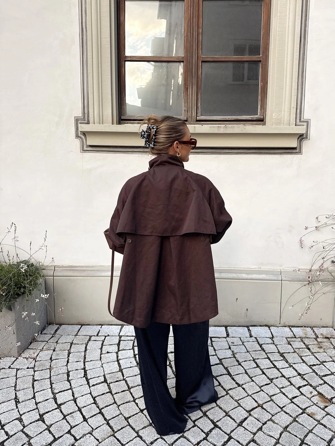Brown cape-like jacket with black wide trousers and cream tote