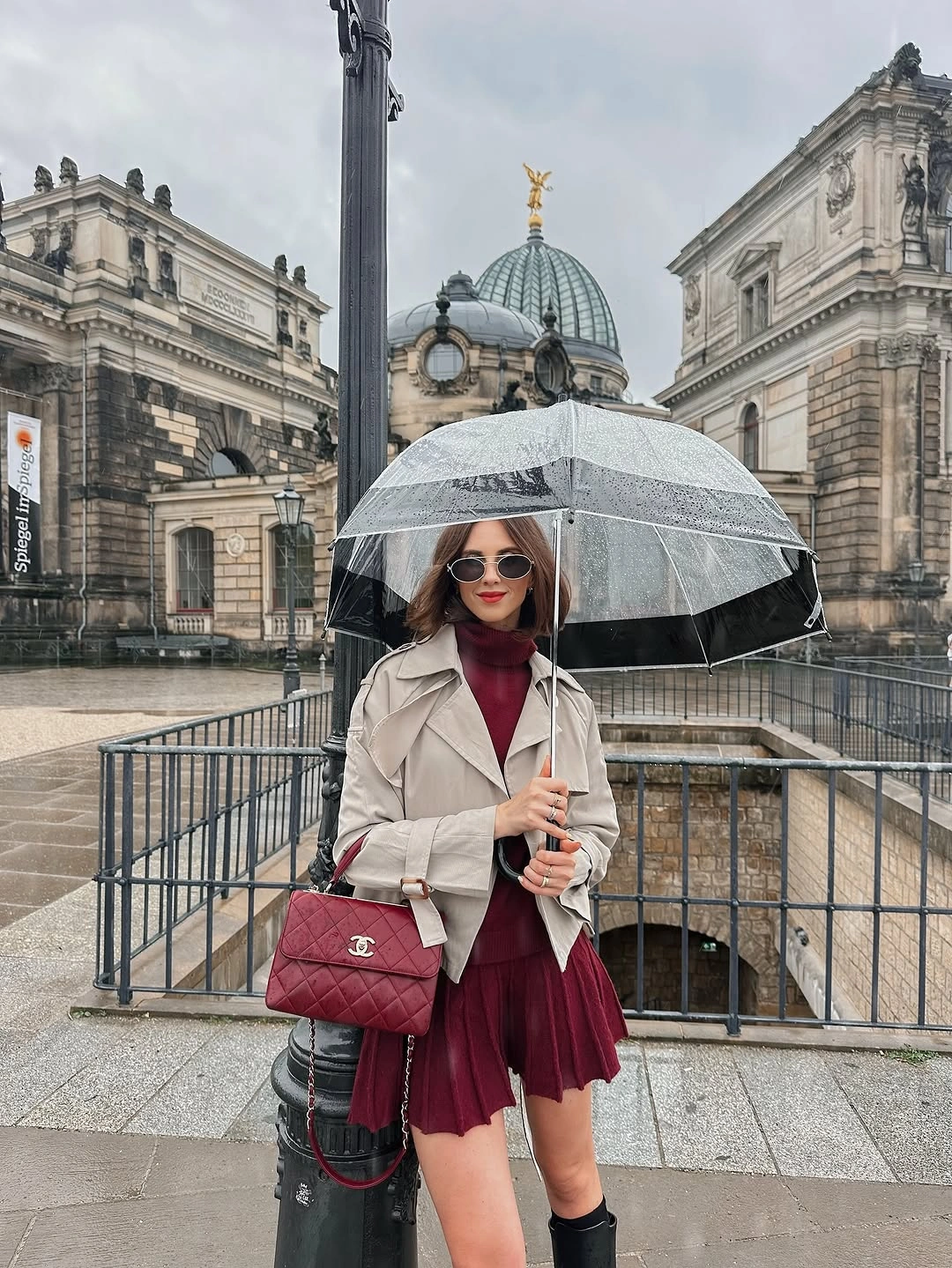 Light trench over burgundy pleated dress and tall black boots