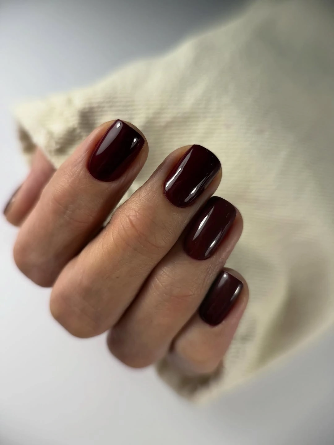 Very dark burgundy short rounded-square nails on cream fabric