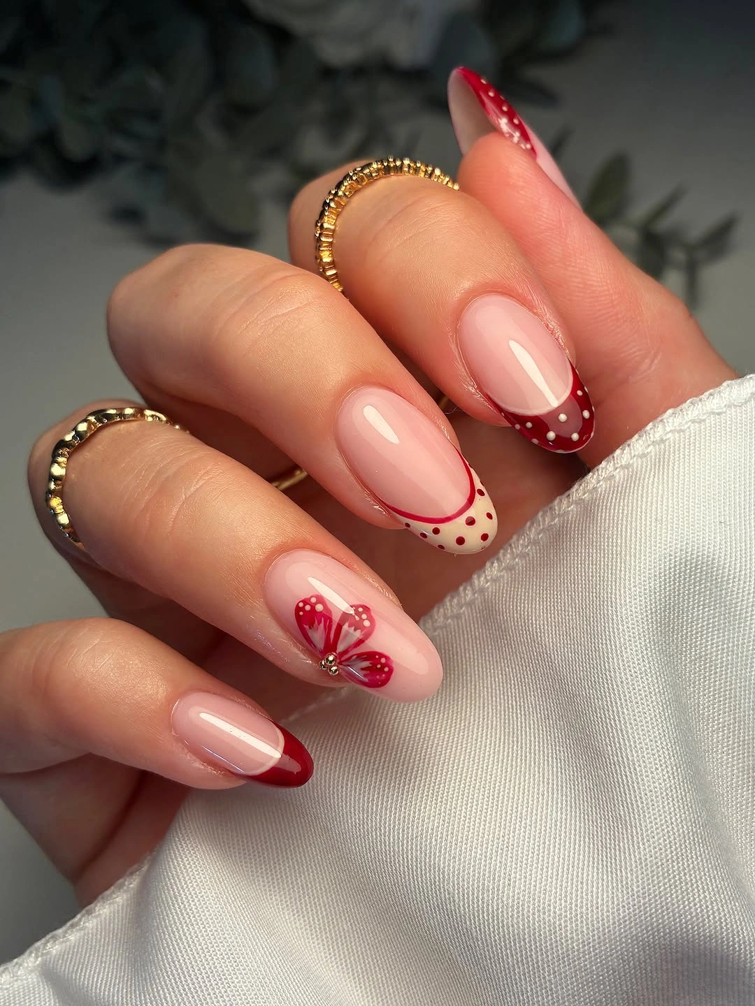 Nude-pink almond nails with red tips dots and butterfly-like detail