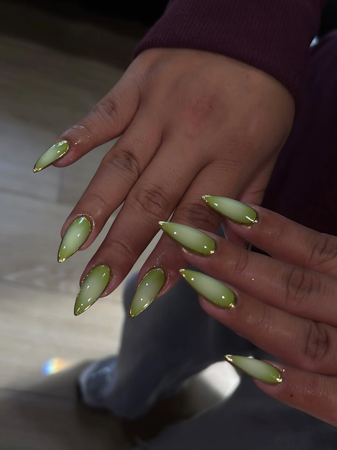 Green almond nails with lighter centers and fine gold-colored outlines
