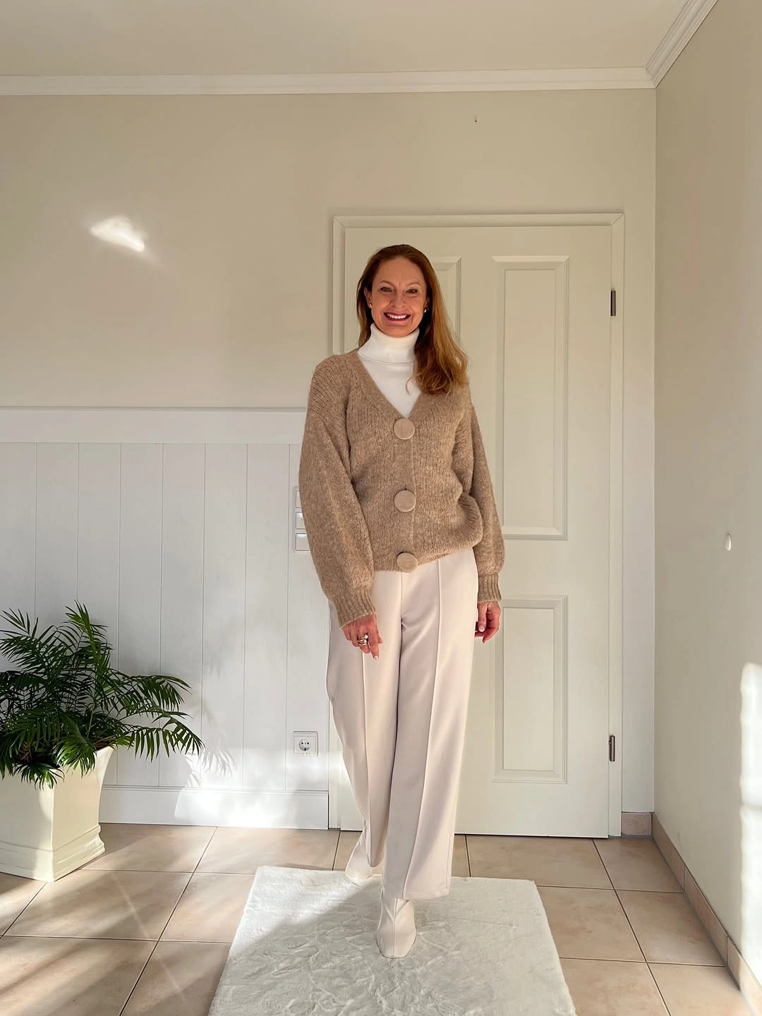 Beige cardigan high-neck top trousers and white sneakers indoors