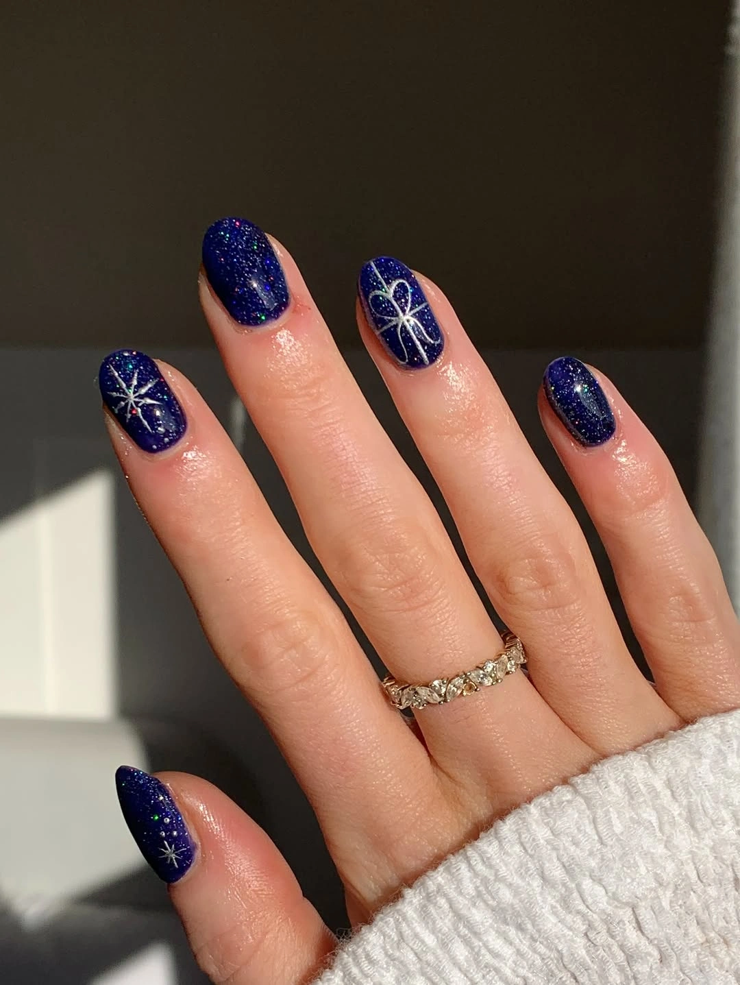 Oval navy sparkle nails with white starbursts and gift bow