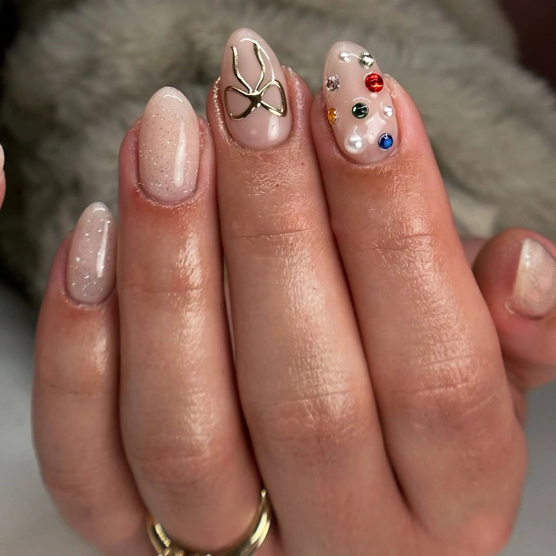 Short nude shimmer nails with gold bow and multicolored accents