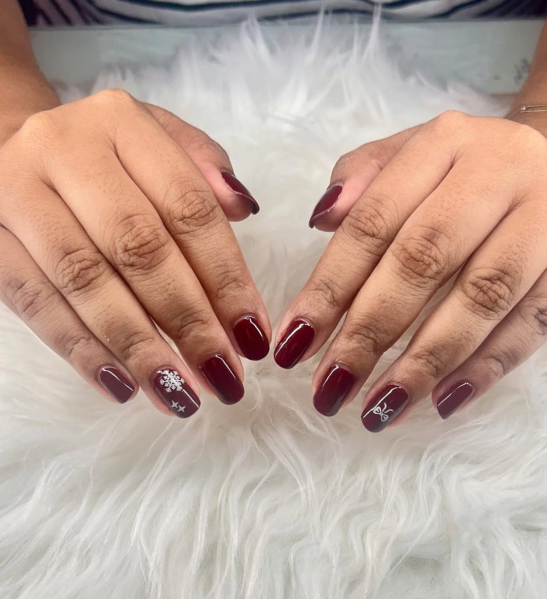 Short burgundy and mauve nails with small white festive motifs