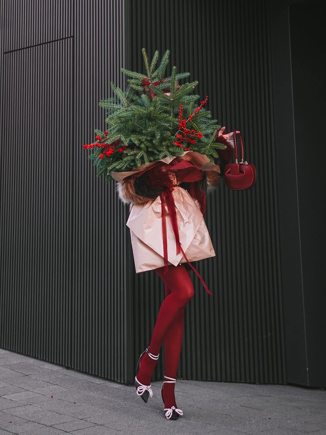 Deep red tights handbag and bow shoes beside wrapped tree