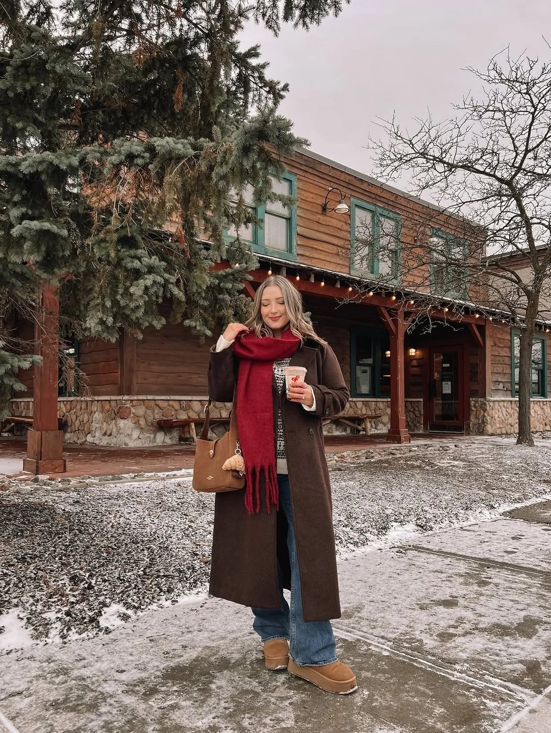 Brown long coat red scarf jeans and tan boots in snow
