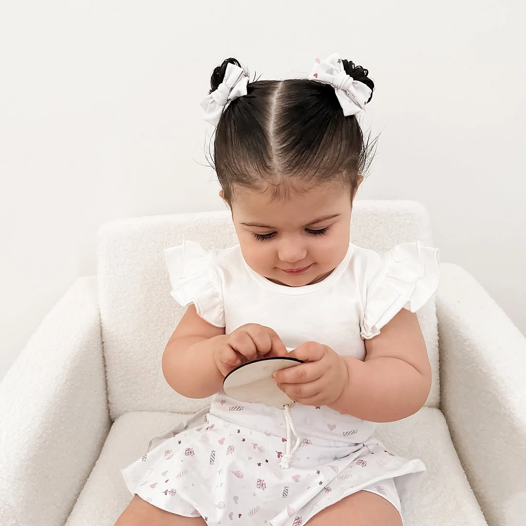 Child wears white ruffled top with two white hair bows