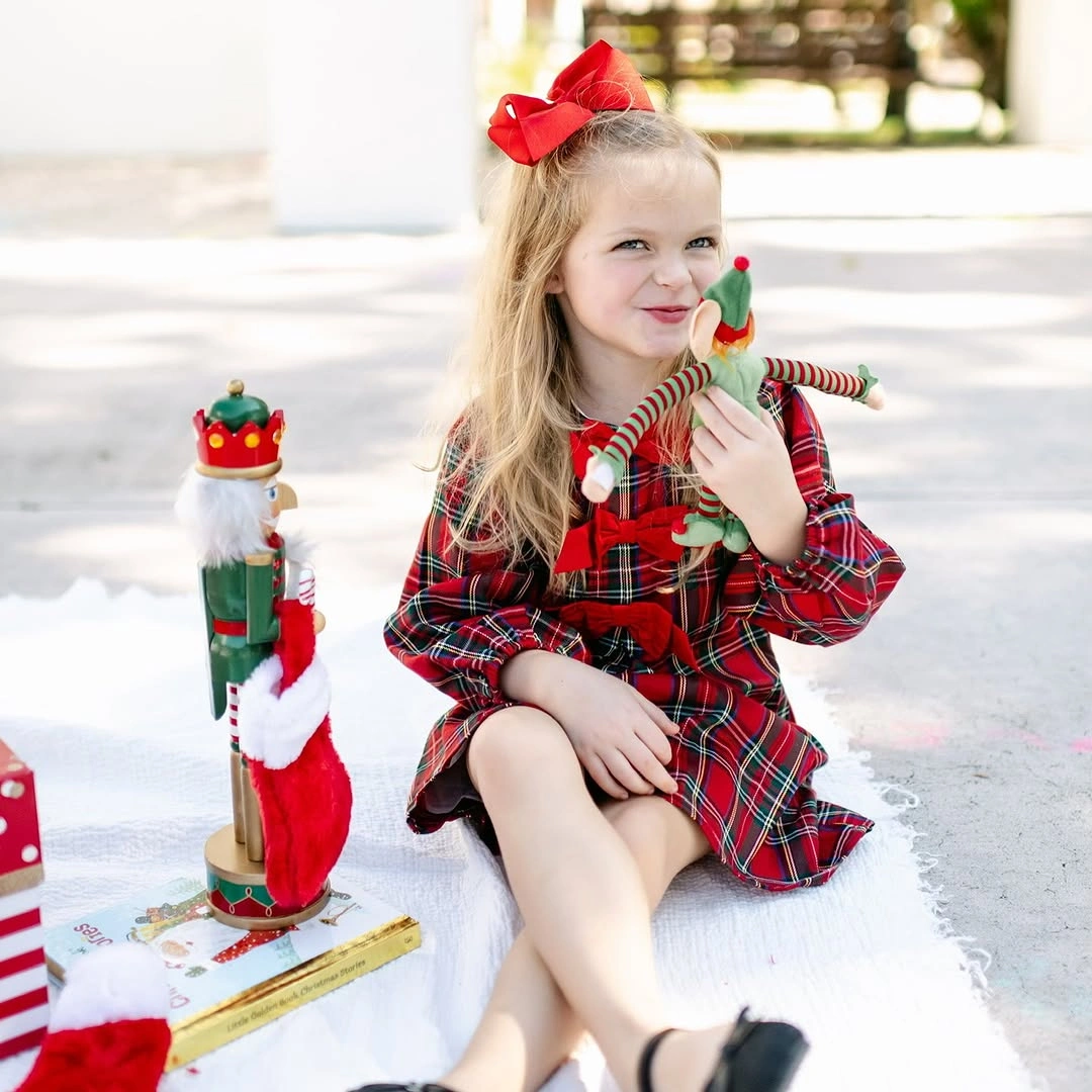 Child wears plaid dress with red bow and waist detail