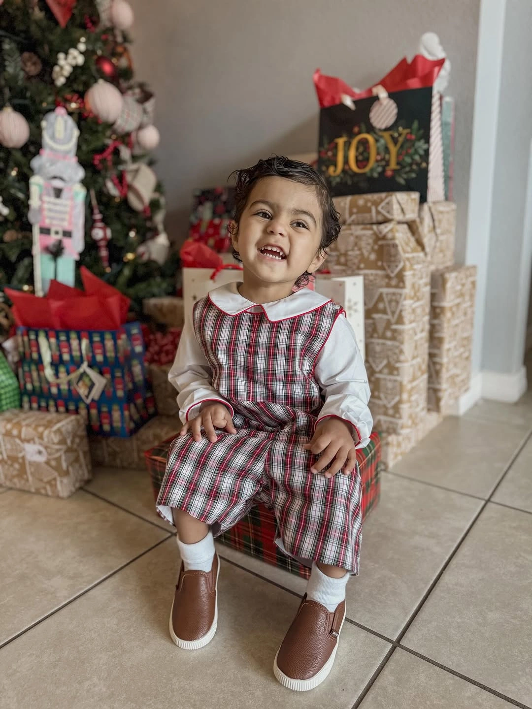 Child wears plaid jumper dress over white collared shirt
