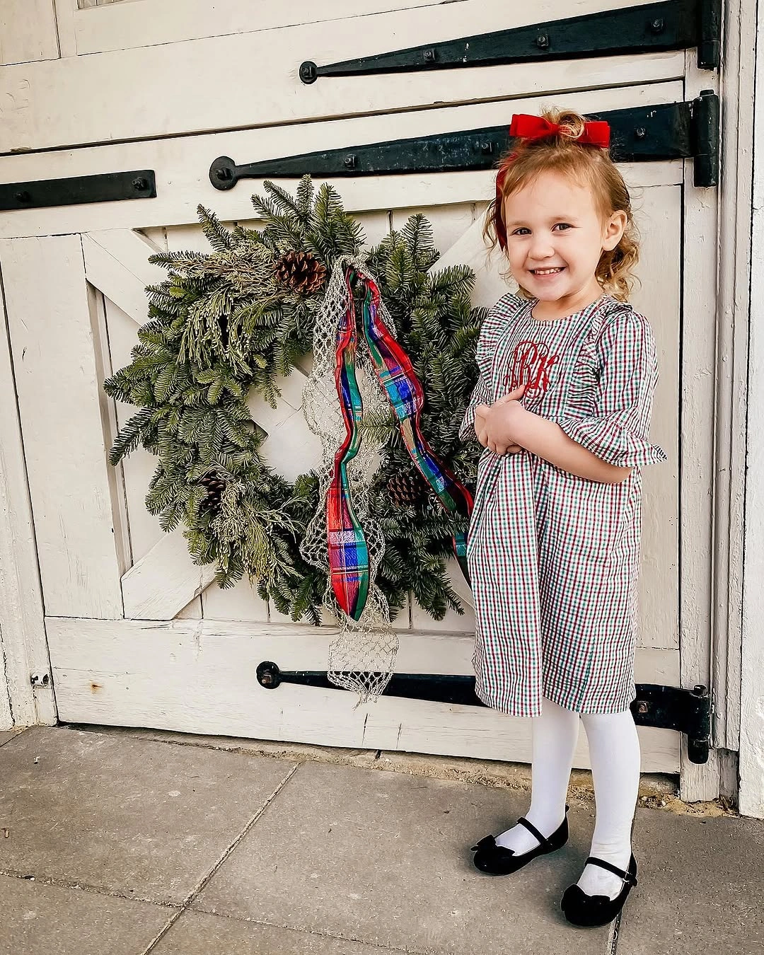 Child wears fine checked dress with red bow and tights