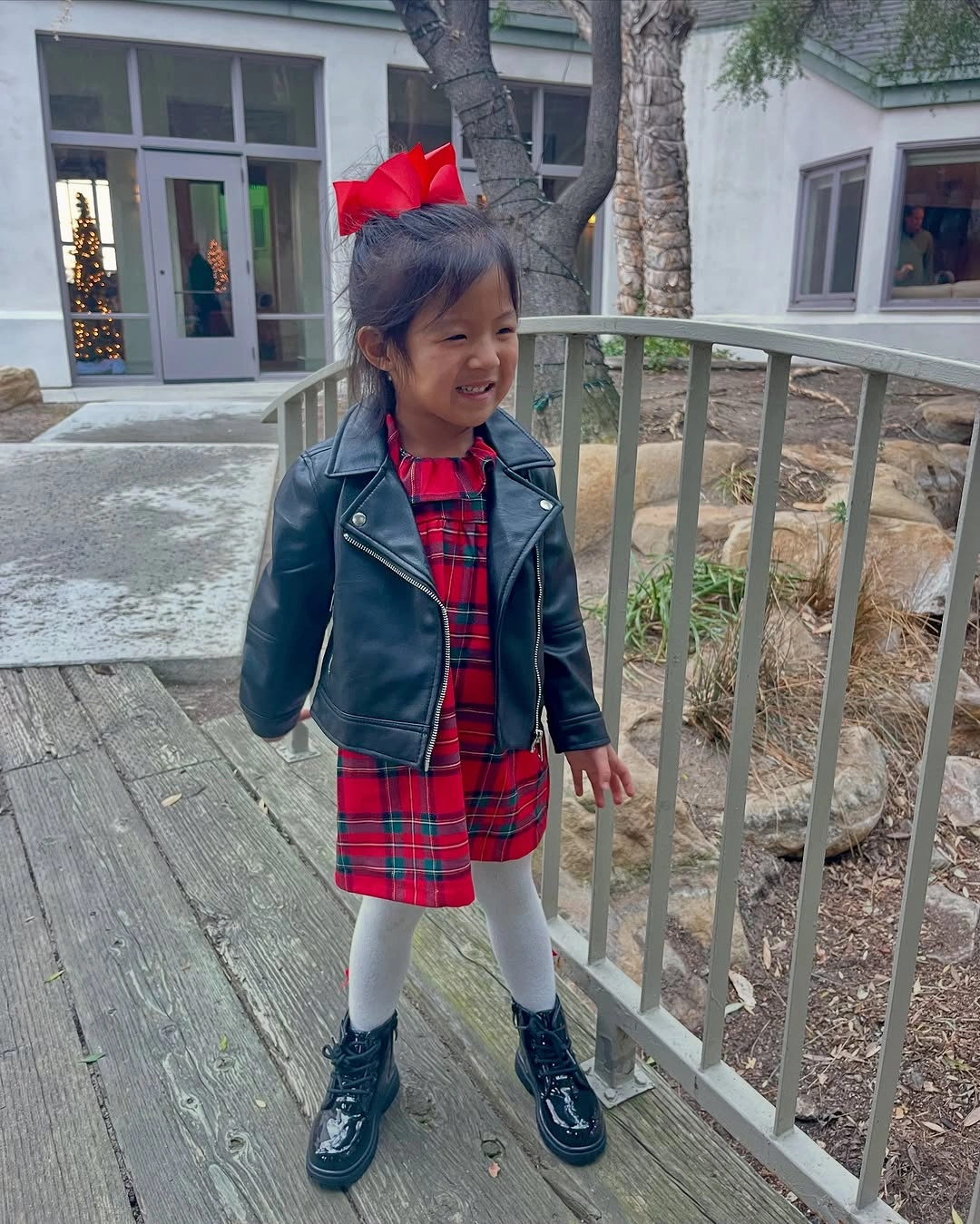 Child wears red plaid dress with black jacket and boots