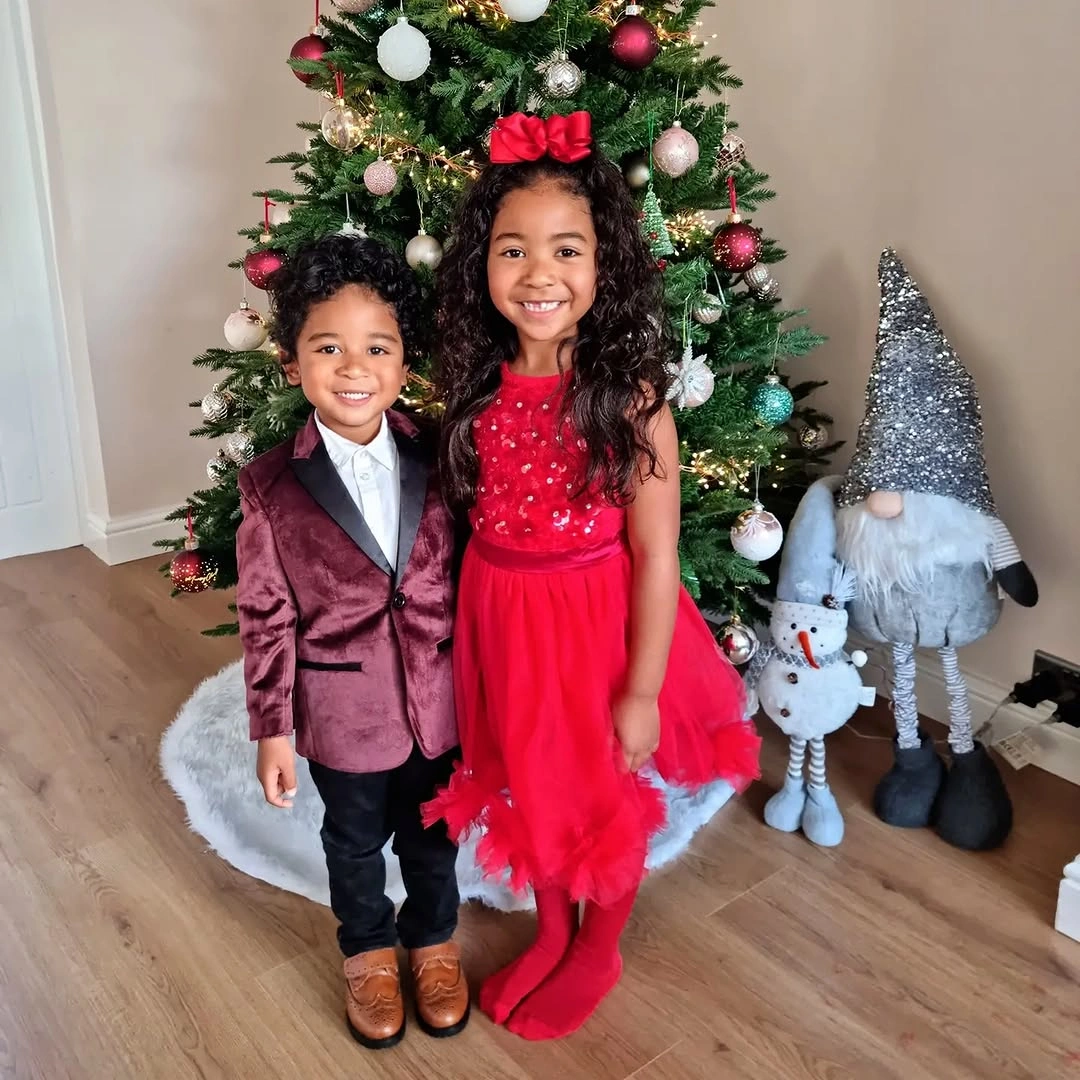 Two children wear burgundy blazer and full red dress