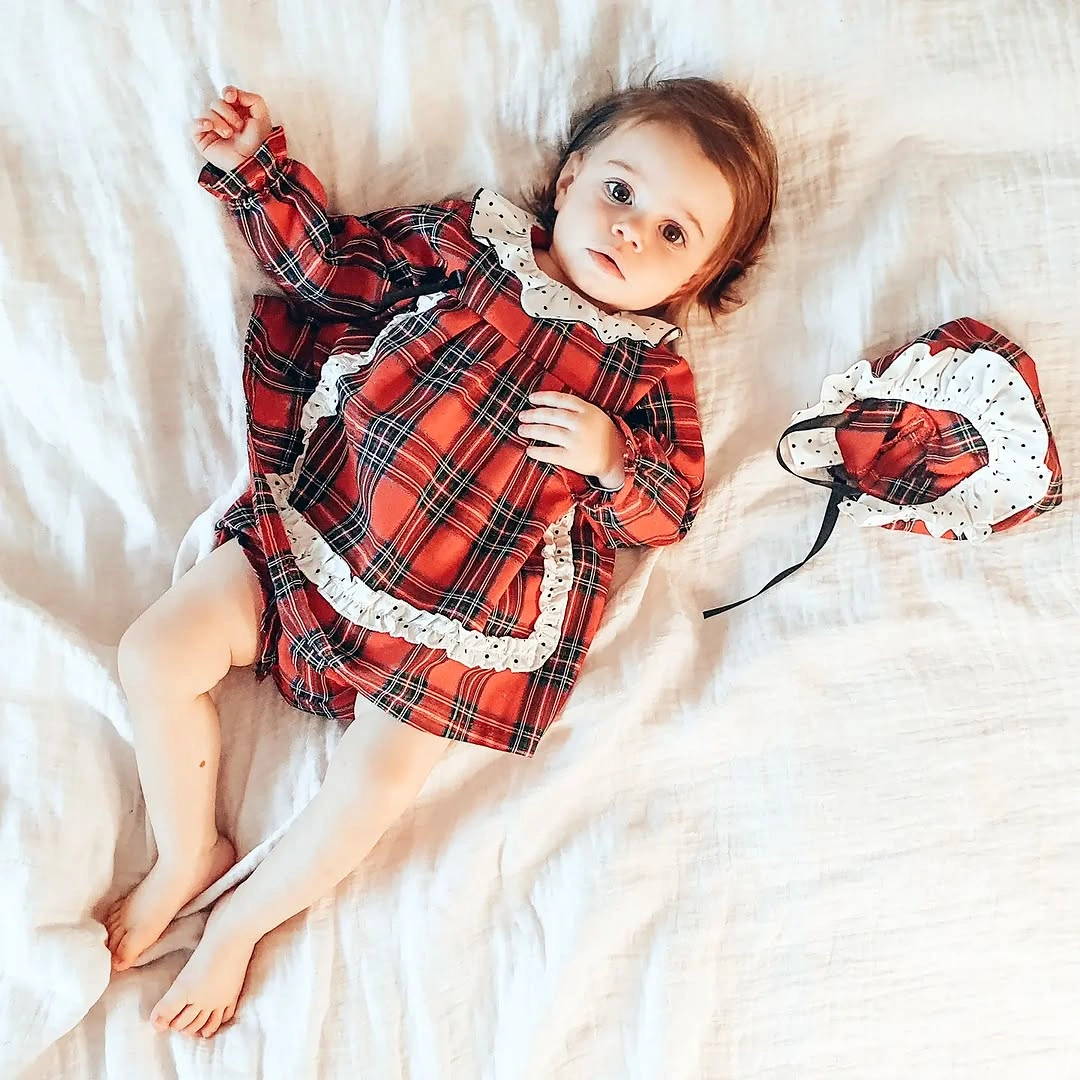 Child wears skirted red plaid one-piece with white ruffles