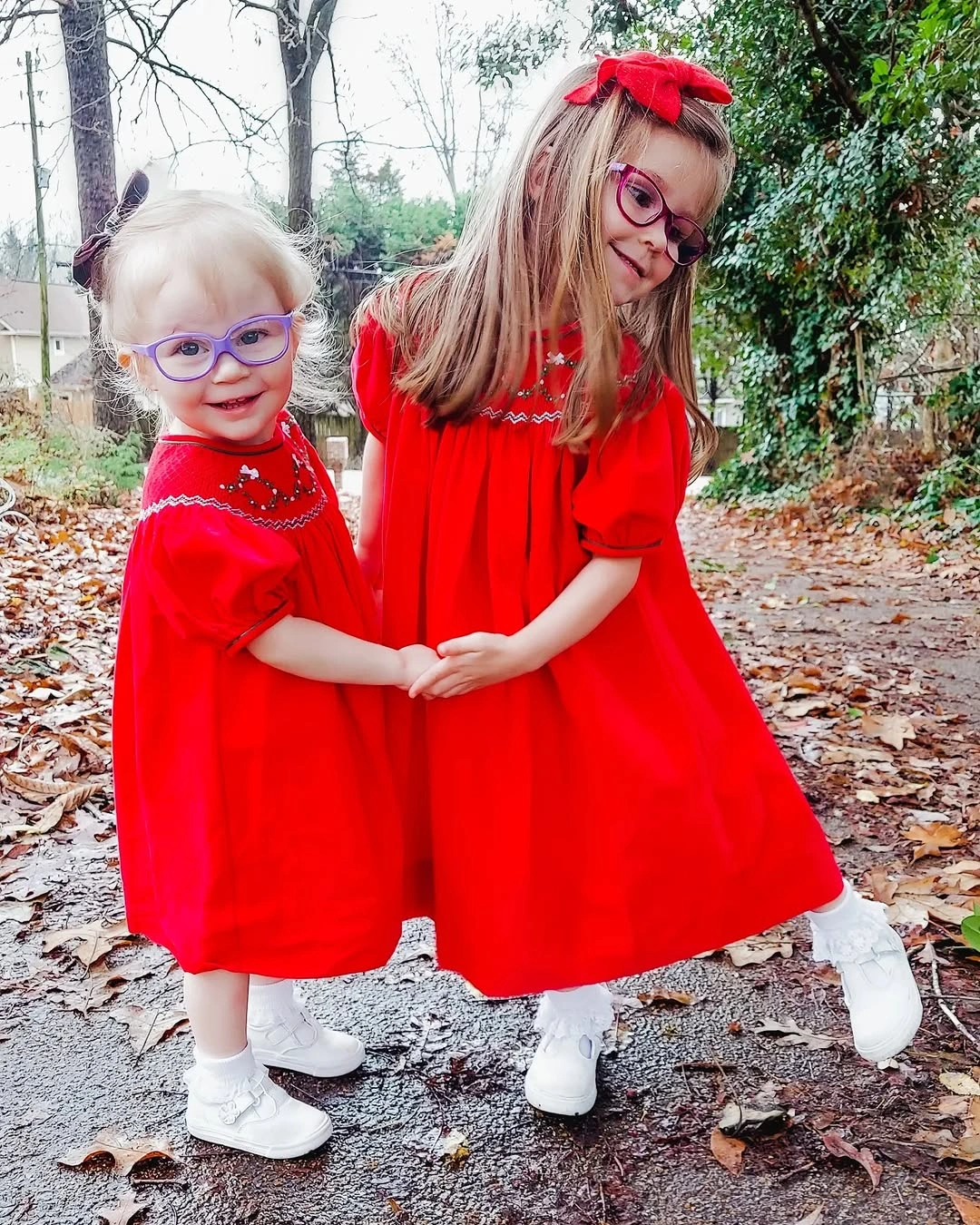 Two children wear matching bright red dresses and white shoes
