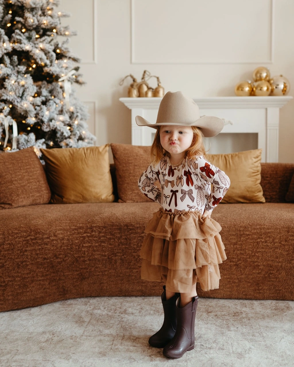Child wears cowboy hat, printed blouse, tiered skirt, and boots