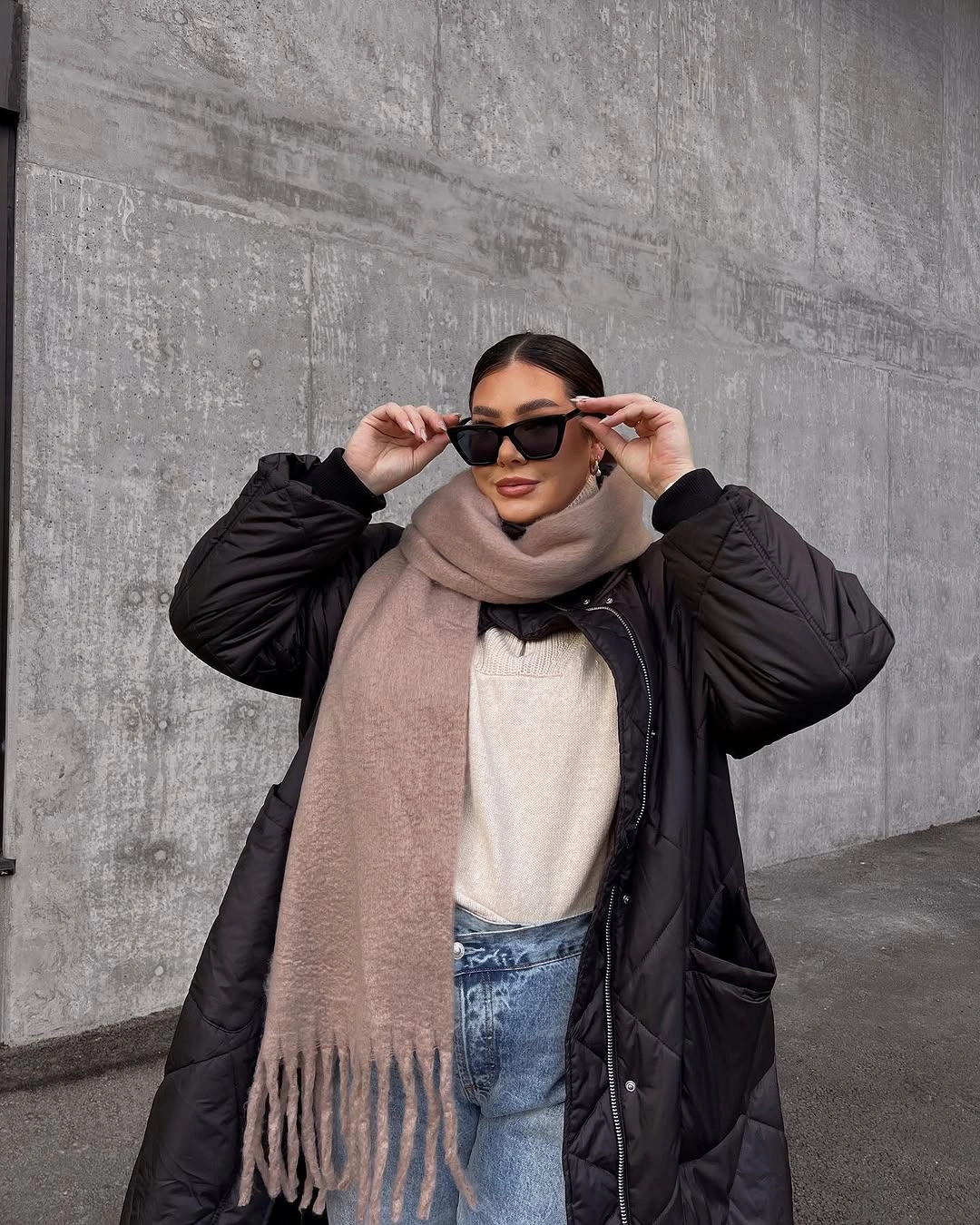 long black puffer, beige scarf, white top, blue jeans and dark sunglasses