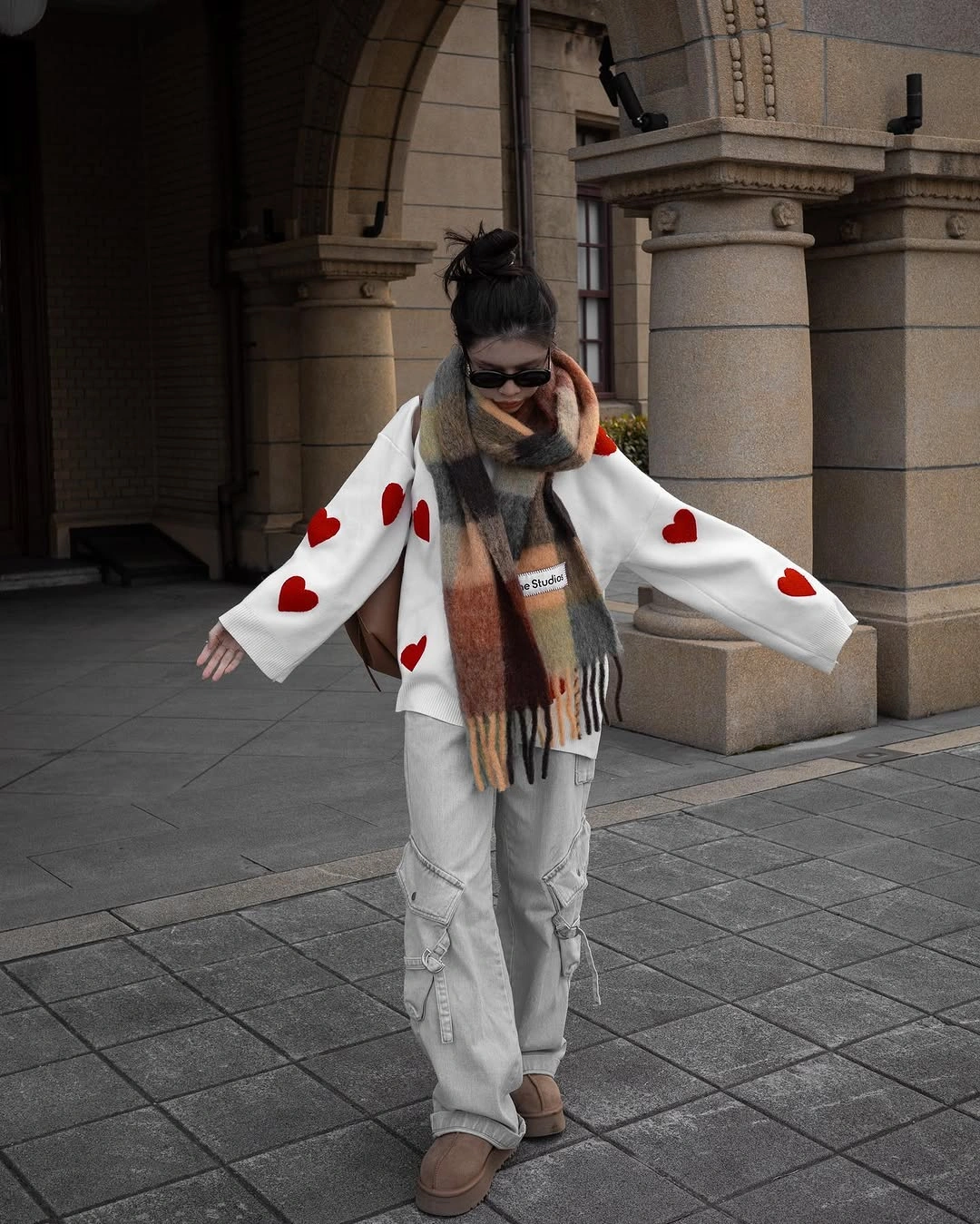 white cardigan with red heart motifs, gray loose trousers and striped scarf