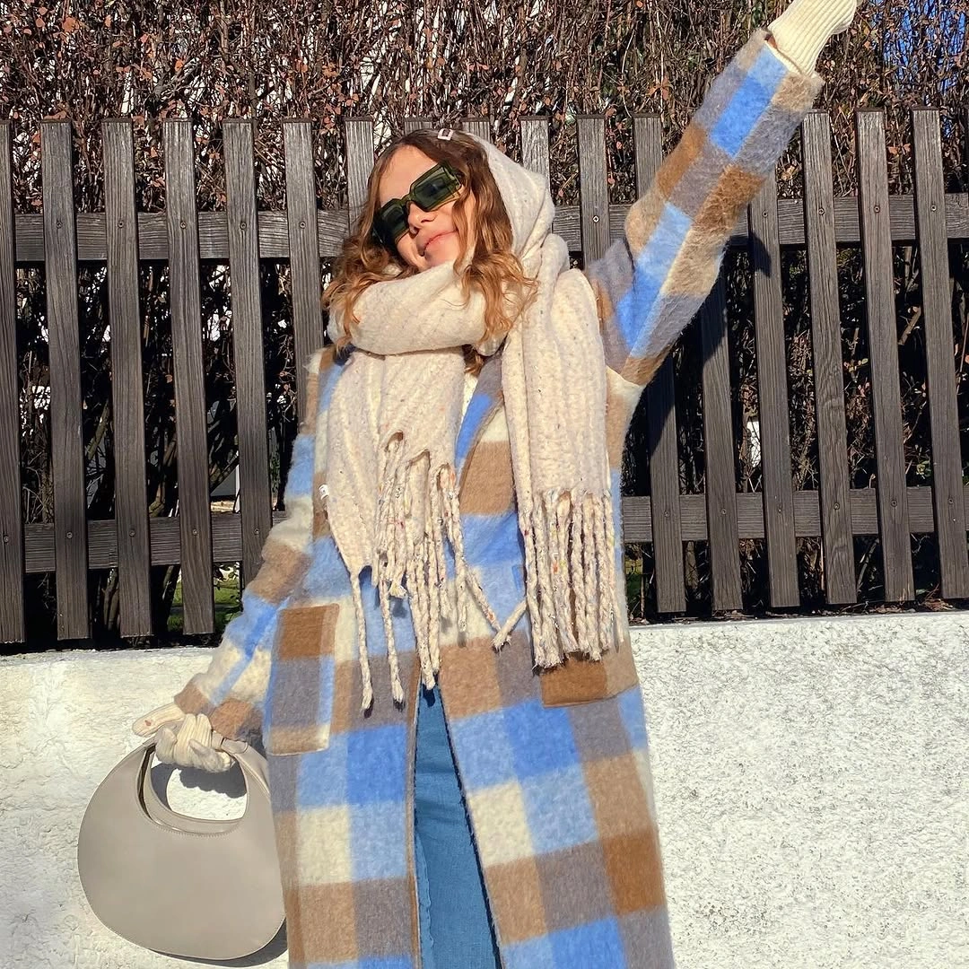large blue-and-tan plaid fringe scarf over cream layers with a rounded bag