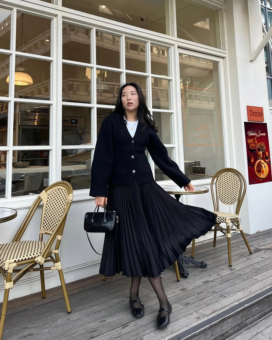 black top, pleated black midi skirt, black shoes and small structured bag