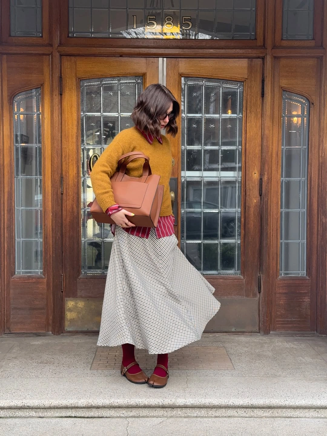 Mustard sweater with striped shirt, checked midi skirt, and dark red tights