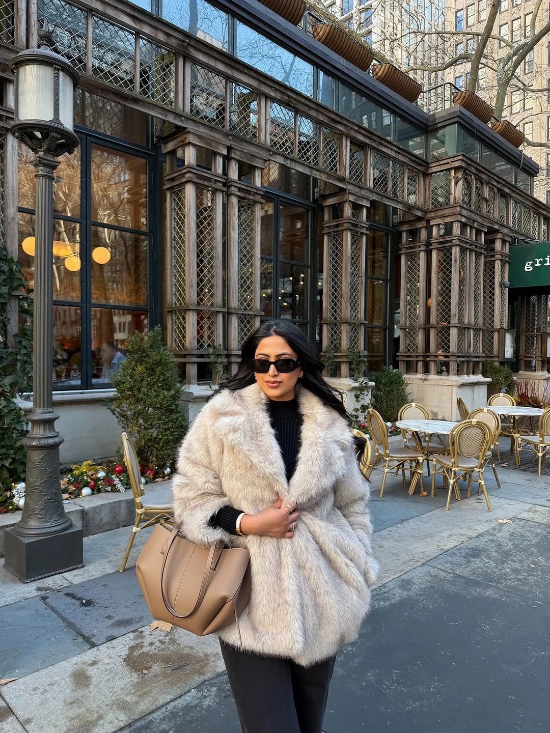 Beige faux-fur coat over a black outfit with a light-brown bag
