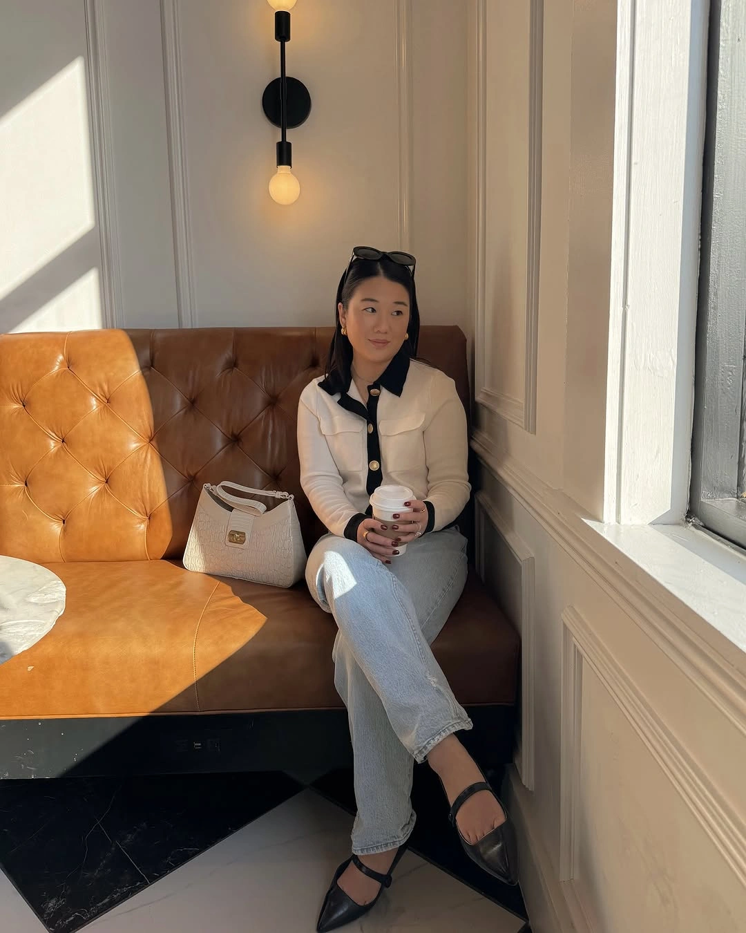 White cardigan with dark collar, light jeans, black shoes, and white bag