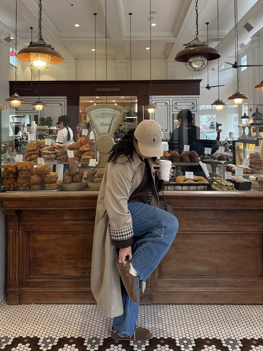 Long beige coat with white sweater, blue jeans, and beige cap