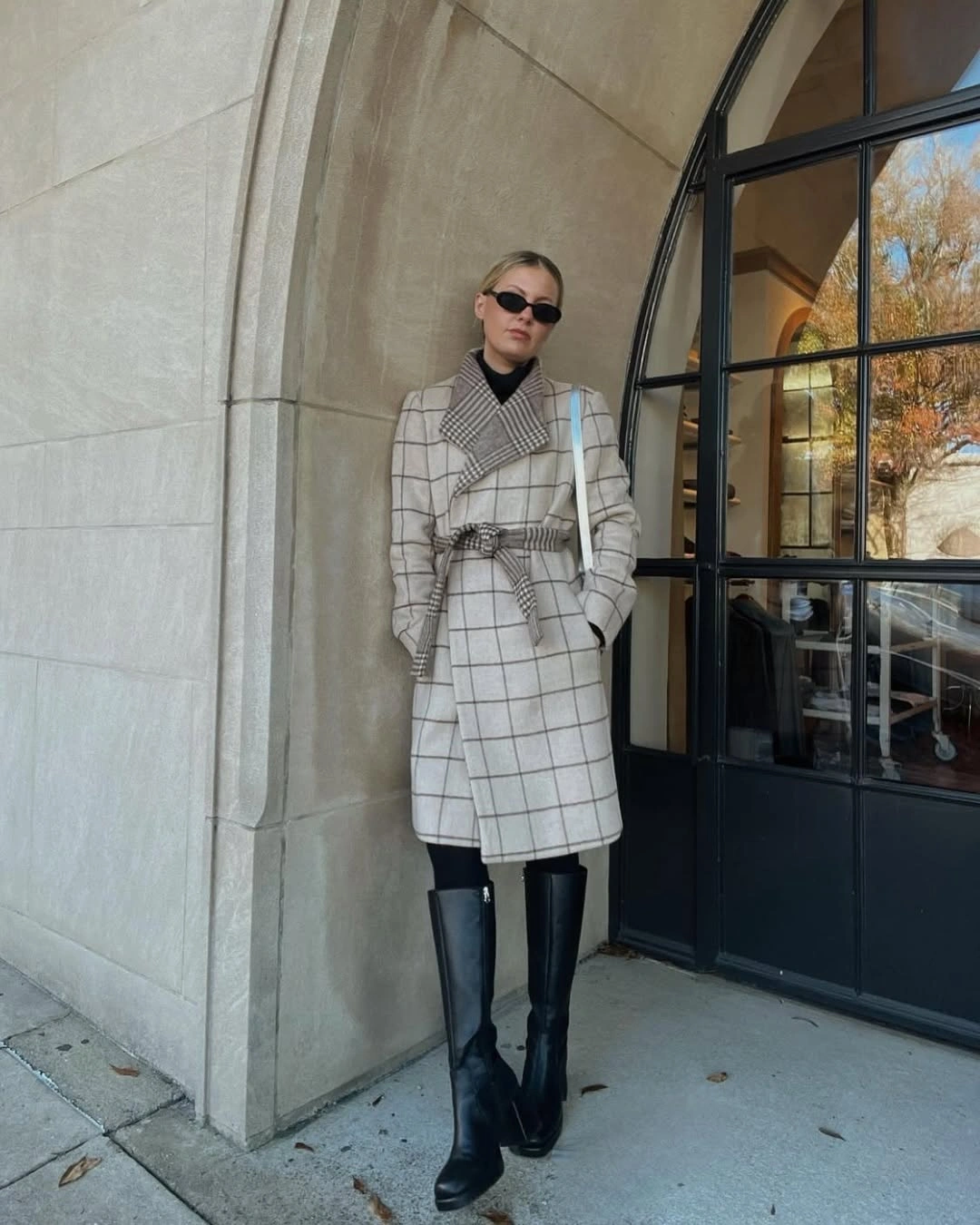 Cream and gray belted plaid coat with black turtleneck and boots