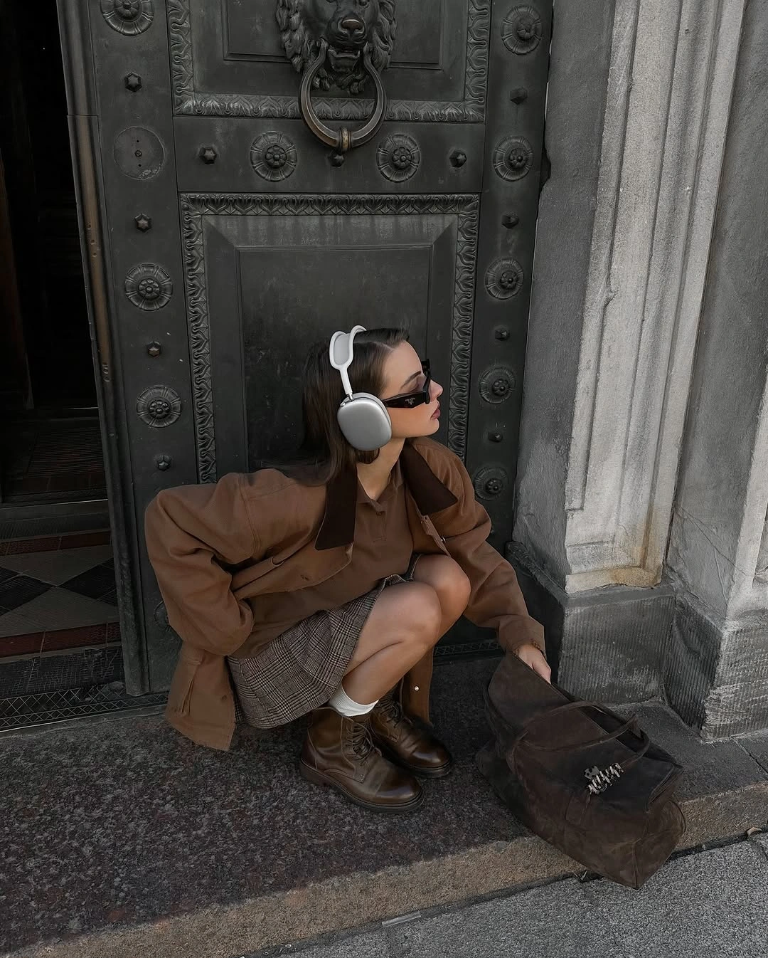 Brown jacket, plaid short skirt, brown boots, headphones, and dark bag