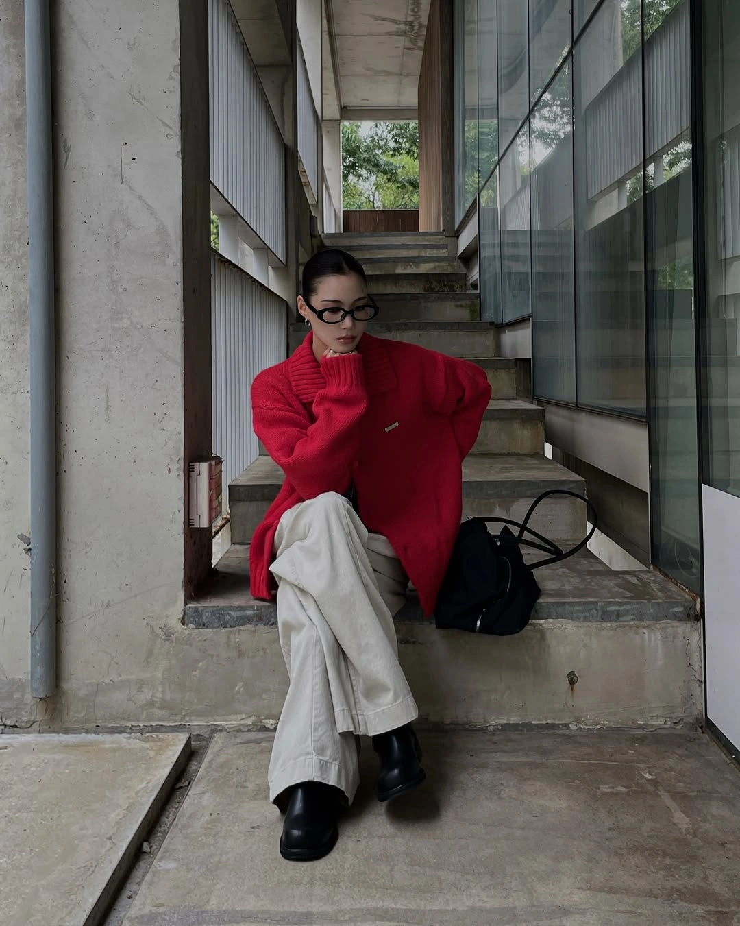 Red oversized sweater, pale trousers, black boots, and black bag